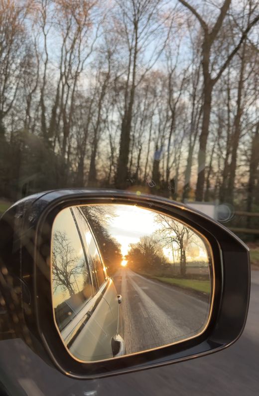 Sunset reflected in a car wing mirror on a quiet tree-lined road